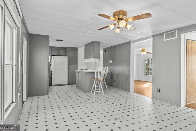 kitchen featuring a breakfast bar, wood walls, ceiling fan, gray cabinets, and white fridge