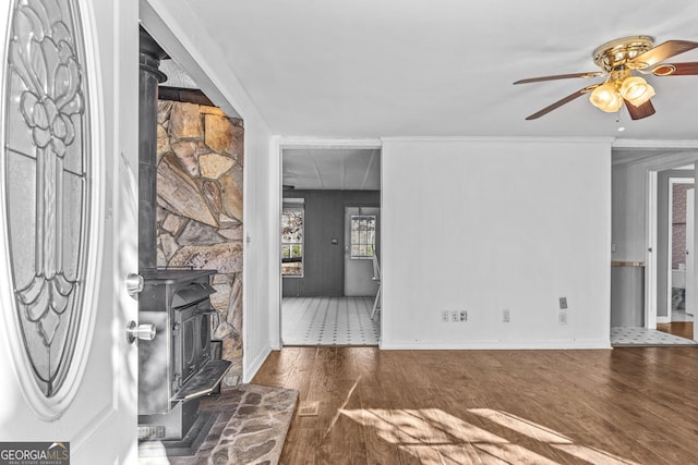 interior space featuring ceiling fan, dark hardwood / wood-style flooring, a wood stove, and ornamental molding