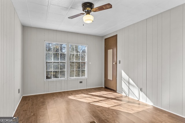 unfurnished room featuring hardwood / wood-style flooring, ceiling fan, and wood walls