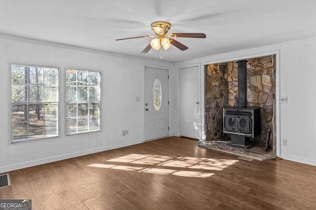 unfurnished living room with a wood stove, ceiling fan, dark hardwood / wood-style flooring, and crown molding