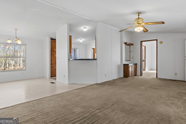 unfurnished living room with ceiling fan with notable chandelier, light colored carpet, and vaulted ceiling