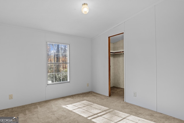 unfurnished bedroom featuring a walk in closet, crown molding, a closet, and light colored carpet