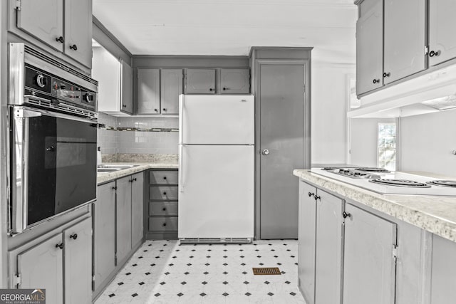 kitchen with tasteful backsplash, gray cabinets, sink, and white appliances