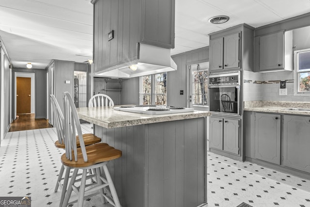 kitchen with black oven, plenty of natural light, gray cabinets, and island exhaust hood