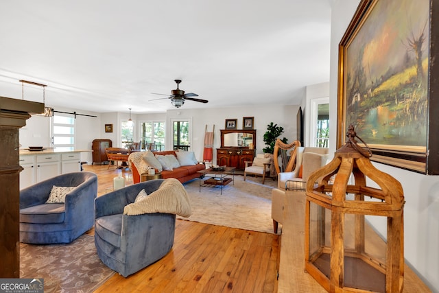 living room with light wood-type flooring, a barn door, and ceiling fan