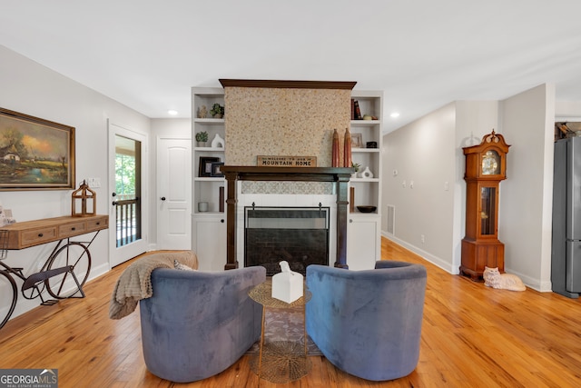 living room featuring a tile fireplace, light hardwood / wood-style floors, and built in shelves