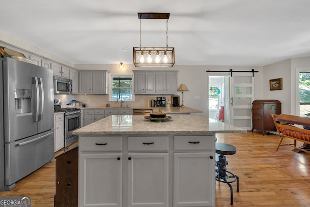 kitchen with gray cabinets, light hardwood / wood-style floors, a kitchen bar, a barn door, and appliances with stainless steel finishes