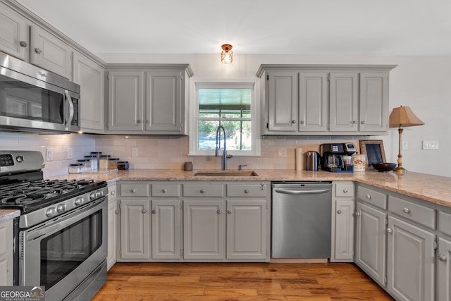 kitchen with appliances with stainless steel finishes, light wood-type flooring, sink, and gray cabinetry