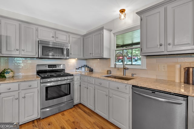 kitchen featuring light hardwood / wood-style floors, backsplash, light stone countertops, stainless steel appliances, and sink