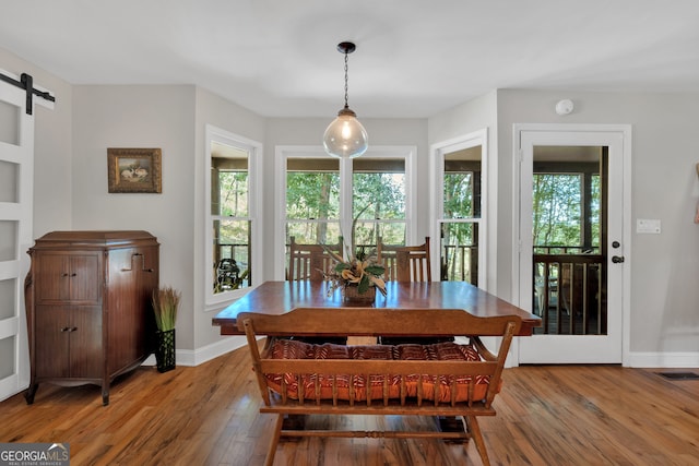 dining room with a barn door, a healthy amount of sunlight, and hardwood / wood-style flooring