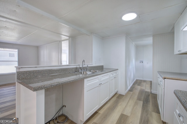 kitchen with white cabinets, light hardwood / wood-style floors, wooden walls, and sink