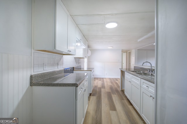 kitchen featuring wood walls, light hardwood / wood-style floors, white cabinetry, and sink