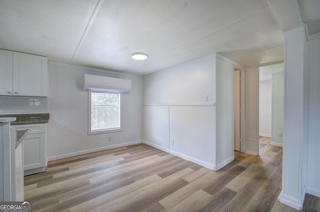 unfurnished dining area with a textured ceiling, light hardwood / wood-style flooring, and a wall mounted air conditioner