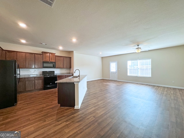 kitchen featuring an island with sink, black appliances, dark wood-type flooring, and sink