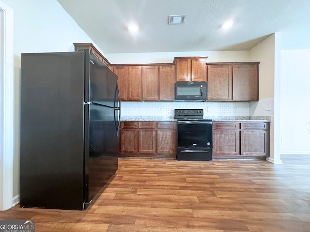 kitchen with light wood-type flooring, black appliances, light stone counters, and tasteful backsplash