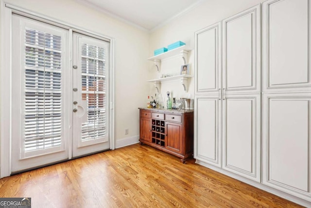 bar with ornamental molding, light wood-type flooring, french doors, and a wealth of natural light