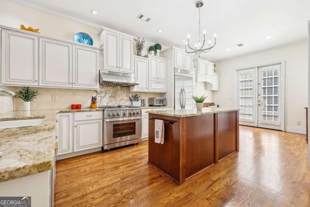 kitchen featuring premium appliances, pendant lighting, a center island, sink, and white cabinetry