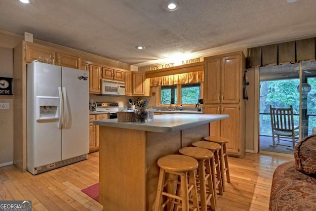 kitchen featuring a breakfast bar, white appliances, light hardwood / wood-style floors, and a center island