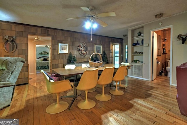 dining area featuring light hardwood / wood-style floors, a textured ceiling, built in shelves, wooden walls, and ornamental molding