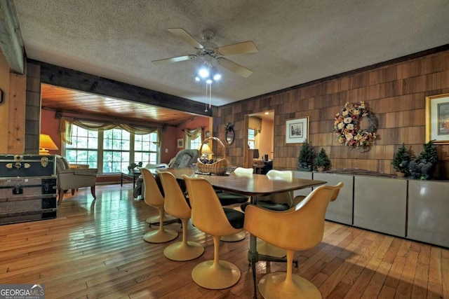 dining area with a textured ceiling, wood walls, beam ceiling, and light hardwood / wood-style flooring