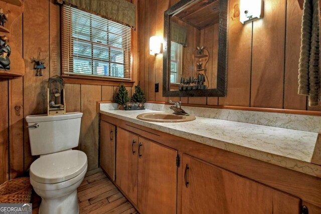 bathroom with vanity, wooden walls, toilet, and hardwood / wood-style flooring