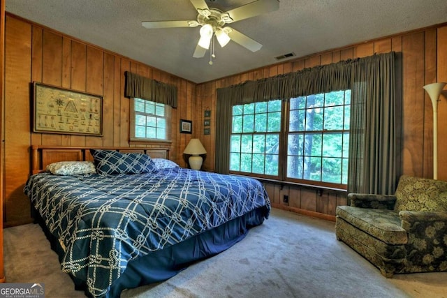 carpeted bedroom featuring ceiling fan, a textured ceiling, and wood walls