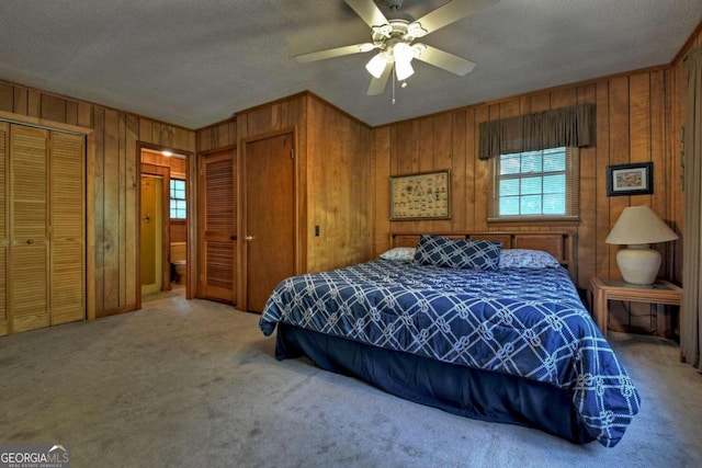 bedroom with ceiling fan, wooden walls, two closets, and carpet