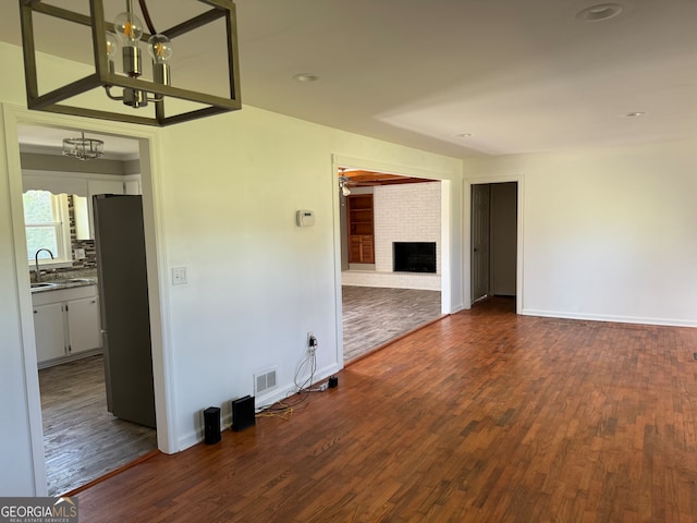 unfurnished room featuring a notable chandelier, a fireplace, sink, and dark hardwood / wood-style flooring