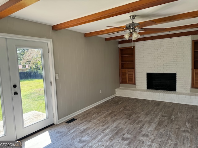 unfurnished living room featuring beamed ceiling, dark wood-type flooring, and a healthy amount of sunlight