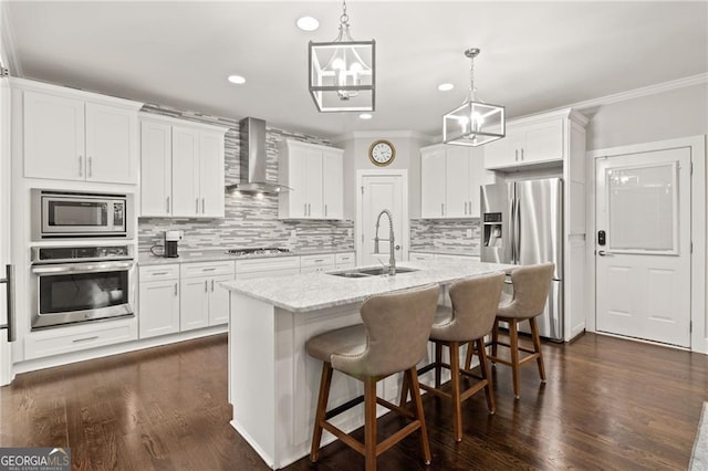 kitchen with white cabinets, an island with sink, stainless steel appliances, and wall chimney range hood