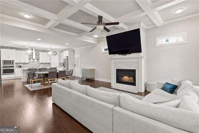 living room featuring ceiling fan, dark wood-type flooring, coffered ceiling, a fireplace, and crown molding