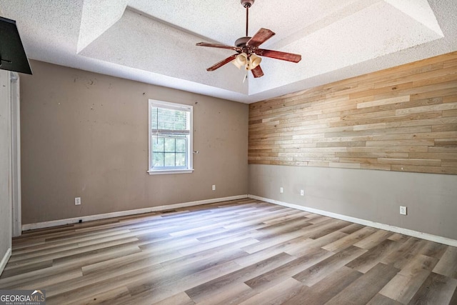 unfurnished room featuring a textured ceiling, ceiling fan, light hardwood / wood-style floors, and a raised ceiling