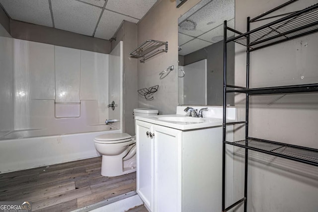 full bathroom featuring a drop ceiling, hardwood / wood-style floors, toilet, shower / bathing tub combination, and vanity