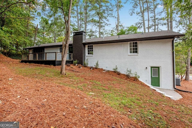 rear view of house featuring a chimney, brick siding, a deck, and central AC