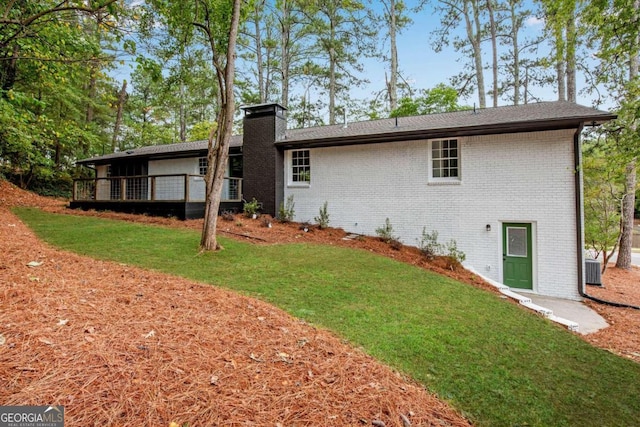 back of property featuring cooling unit, a chimney, brick siding, a deck, and a yard