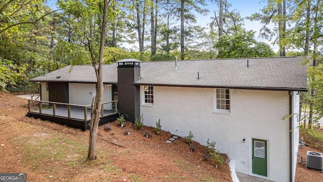 rear view of house with a chimney, a shingled roof, cooling unit, a wooden deck, and brick siding