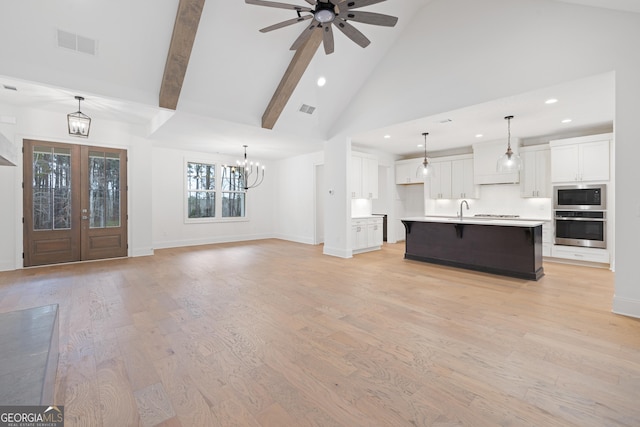 unfurnished living room featuring light wood-type flooring, sink, high vaulted ceiling, and french doors