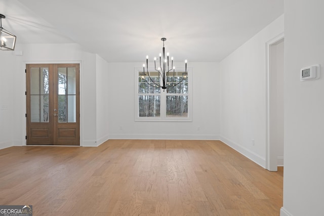 unfurnished dining area featuring a notable chandelier, plenty of natural light, french doors, and light wood-type flooring