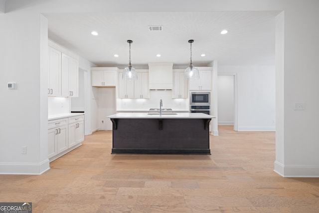 kitchen with built in microwave, white cabinetry, an island with sink, and stainless steel oven