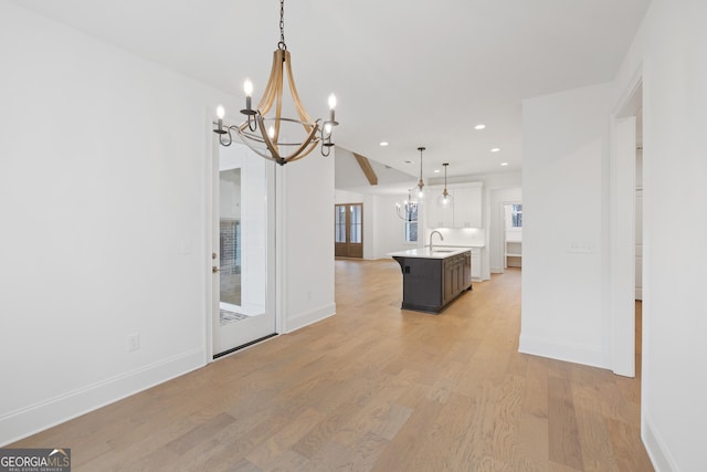 kitchen featuring sink, an inviting chandelier, decorative light fixtures, a center island with sink, and light wood-type flooring