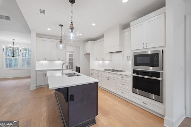 kitchen featuring appliances with stainless steel finishes, a center island with sink, white cabinets, and decorative light fixtures