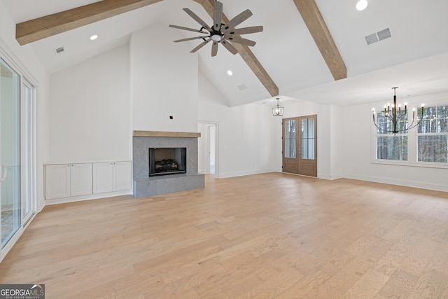 unfurnished living room with beam ceiling, high vaulted ceiling, a fireplace, light hardwood / wood-style floors, and french doors