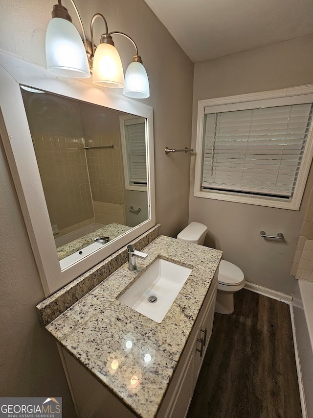 bathroom featuring a tile shower, wood-type flooring, vanity, and toilet