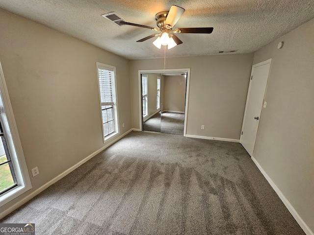 spare room featuring a textured ceiling, carpet flooring, ceiling fan, and a wealth of natural light