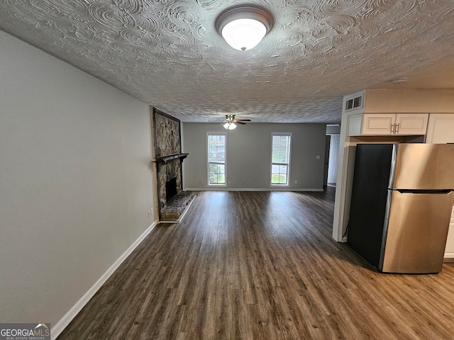 kitchen with white cabinets, stainless steel fridge, wood-type flooring, a textured ceiling, and a fireplace