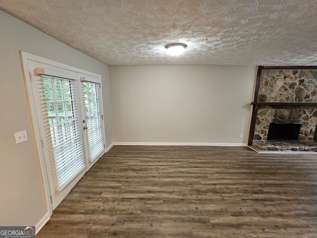 unfurnished living room featuring a stone fireplace, a textured ceiling, and dark hardwood / wood-style flooring