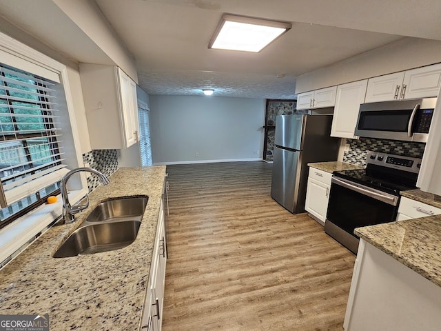 kitchen with appliances with stainless steel finishes, light hardwood / wood-style floors, white cabinetry, light stone countertops, and sink