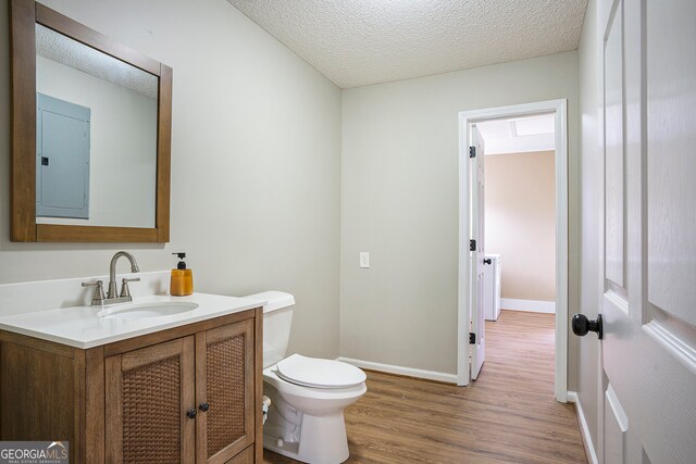 bathroom with toilet, wood-type flooring, vanity, electric panel, and a textured ceiling