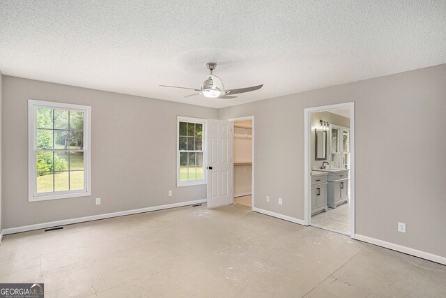 unfurnished bedroom featuring a spacious closet, ensuite bathroom, and a textured ceiling