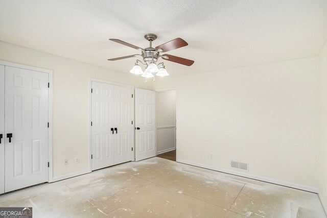 unfurnished bedroom featuring ceiling fan, a textured ceiling, and two closets